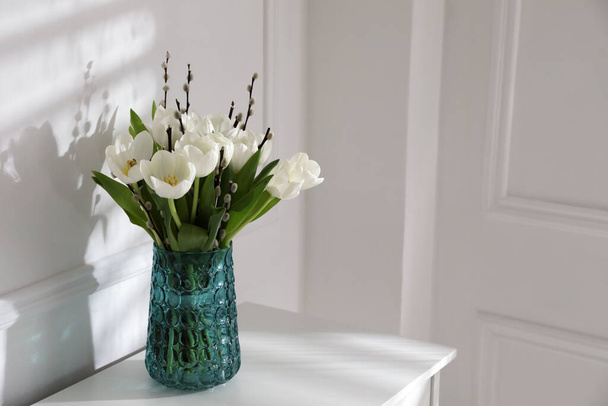 Beautiful bouquet of willow branches and tulips in vase near white wall indoors, space for text - Foto, imagen
