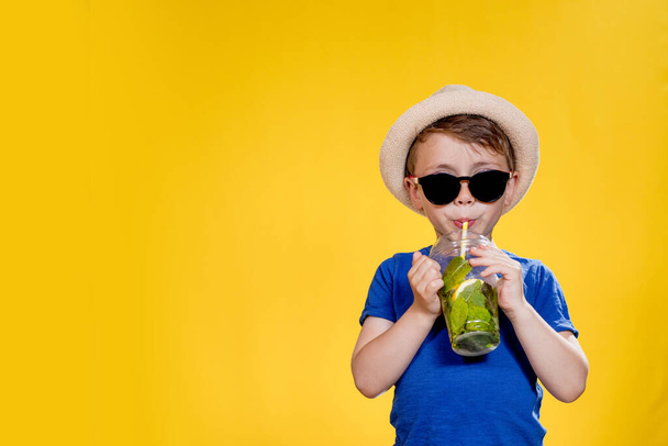 Boy in summer outfit wearing sunglasses and enjoying while drinking a Mojito cocktail. Posing on the yellow background - Zdjęcie, obraz