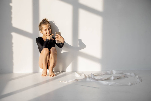 Malá holka sedí s chytrým telefonem ve třídě gymnastiky - Fotografie, Obrázek