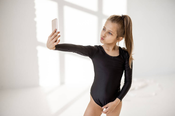 Маленька дівчинка сидить зі смартфоном у класі гімнастики
 - Фото, зображення