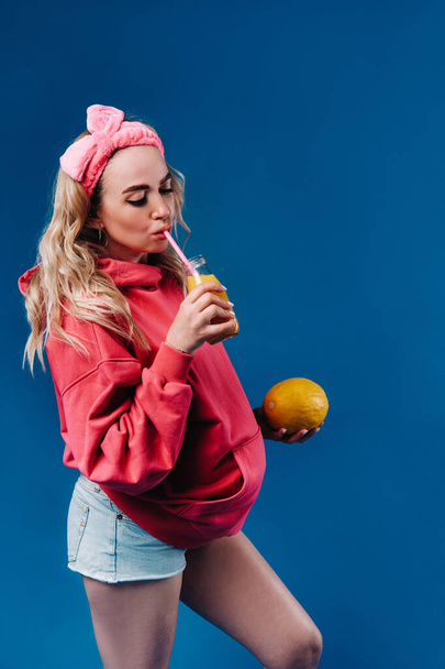 pregnant girl in pink clothes with a bottle of juice and a melon on a blue background. - Fotoğraf, Görsel