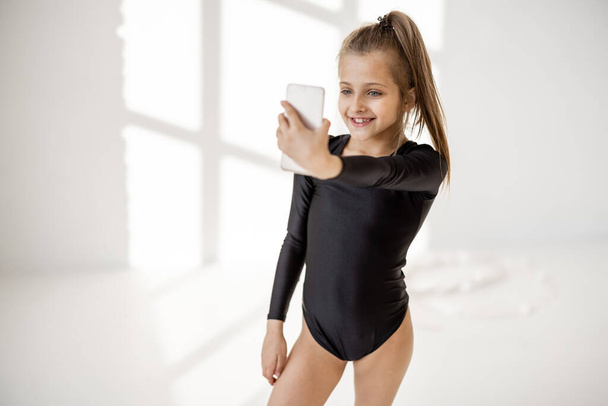 Little girl sitting with smart phone in gymnastics class - Zdjęcie, obraz