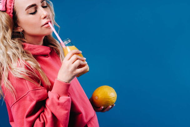 pregnant girl in pink clothes with a bottle of juice and a melon on a blue background. - Фото, зображення