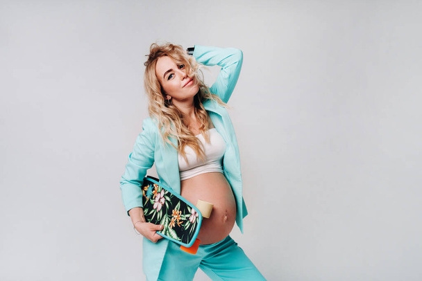 a pregnant girl in turquoise clothes with a skateboard in her hands on a gray background. - Foto, Bild