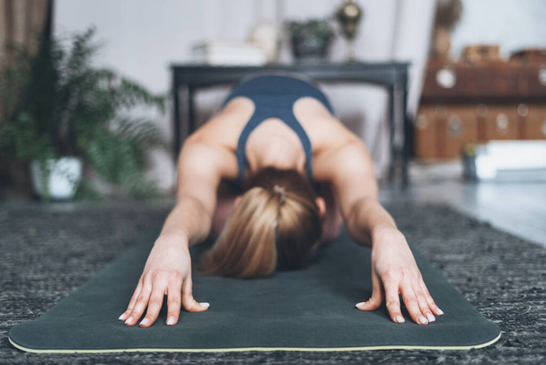 Selective focus on young woman practicing yoga, doing balasana or child pose exercise. Female working out at home, stretching her body while she making sport training indoors, close up hands view - Foto, Imagem