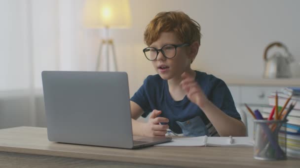 Concept d'enseignement à distance. mignon petit rousse écolier dans lunettes vidéo bavarder avec enseignant via ordinateur portable - Séquence, vidéo