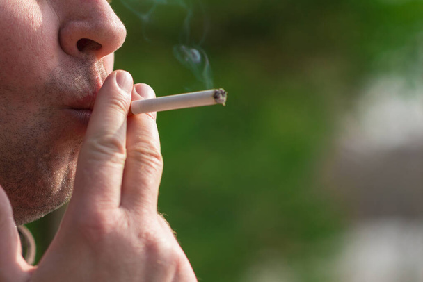 Обрезанный крупным планом мужчина курит сигарету на открытом воздухе.. - Фото, изображение