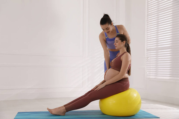 Trainer working with pregnant woman in gym. Preparation for child birth - Zdjęcie, obraz