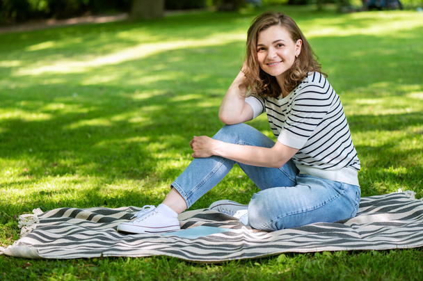 Happy pretty woman resting on blanket in green park - Фото, изображение