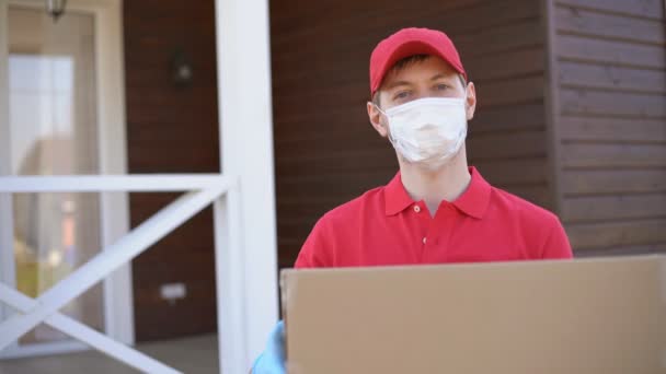 Retrato del repartidor con máscara de seguridad sosteniendo una caja. Servicio en cuarentena. - Imágenes, Vídeo