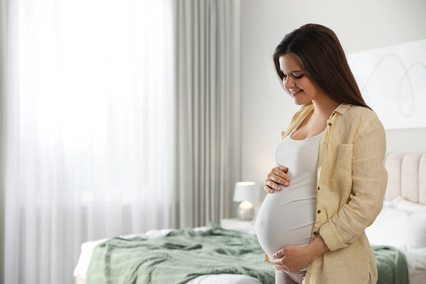 Young happy pregnant woman in bedroom, space for text - Foto, Bild