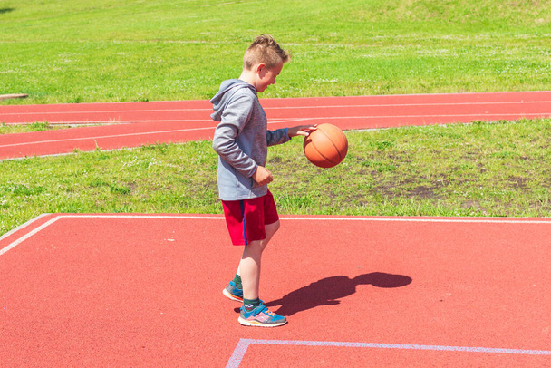 遊び場でのバスケットボール撮影の準備少年は晴れた夏の日に遊び場でバスケットボールの試合でショットを実行します. - 写真・画像