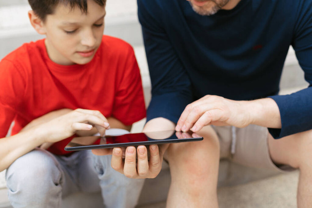 Η έννοια της χρήσης gadgets για την εκπαίδευση ή να περνούν χρόνο με τα παιδιά. Νεαρός πατέρας και γιος σε σκαλιά τσιμεντένιας σκάλας - Φωτογραφία, εικόνα