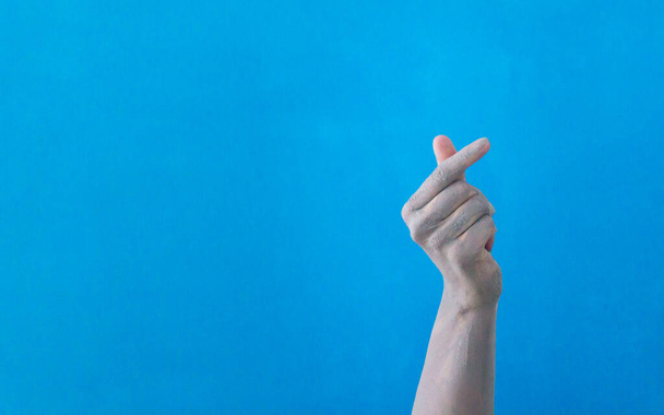 Κορεάτικο σύμβολο αγάπης με τα δάχτυλά σου σε πηλό σε μπλε φόντο. Το χέρι μιας γυναίκας αντιπροσωπεύει μια καρδιά.. - Φωτογραφία, εικόνα