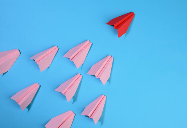 group of pink paper planes follow the first red against a blue background. The concept of uniting a team to achieve goals, a strong leader, a highly effective group, top view - Photo, Image