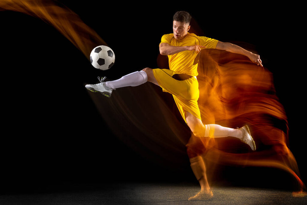 One caucasian male football or soccer player training with ball in mixed light isolated on dark background. Concept of professional sport, active, motion.. - Fotografie, Obrázek