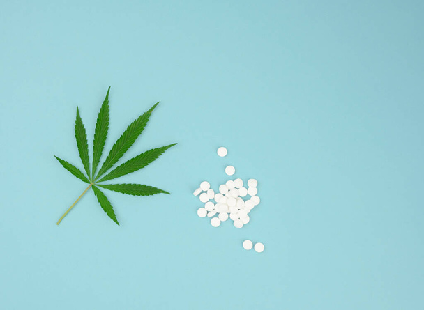 grünes Hanfblatt und weiße Tabletten auf blauem Hintergrund, Konzept der Legalisierung alternativer Behandlungsmethoden, Ansicht von oben - Foto, Bild