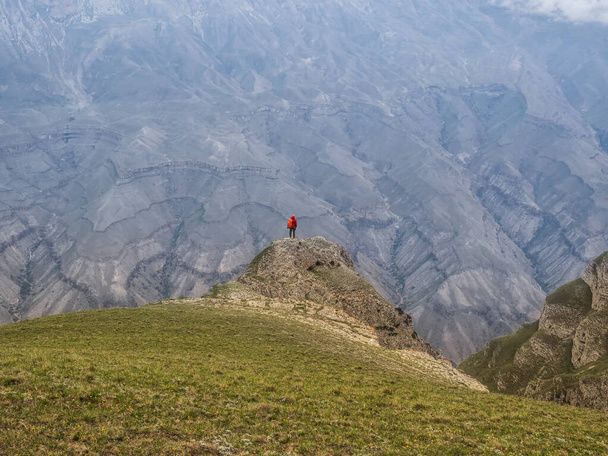 Kleine Silhouette einer Frau mit Rucksack steht mit dem Rücken über der Klippe. Einsamkeit in den Bergen, Alleinreisekonzept. - Foto, Bild