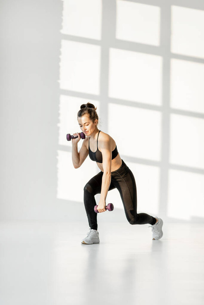 Woman doing cardio with dumbbells at white room - Foto, Bild