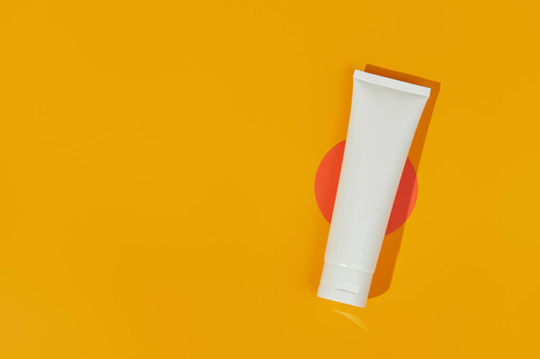 Flat lay top view blank white tube bottle with lotion cream or cleanser on orange background - Фото, изображение