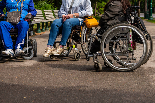 Vista para duas mulheres e um homem pernas sentadas nas cadeiras de rodas. Três pessoas com cadeiras de rodas relaxando no parque no dia ensolarado.  - Foto, Imagem