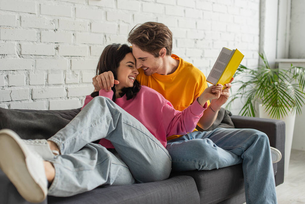 happy young couple hugging and holding book in living room - Fotó, kép