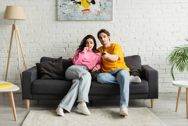 joven apuntando con mando a distancia a la cámara y abrazando novia en la sala de estar - Foto, Imagen