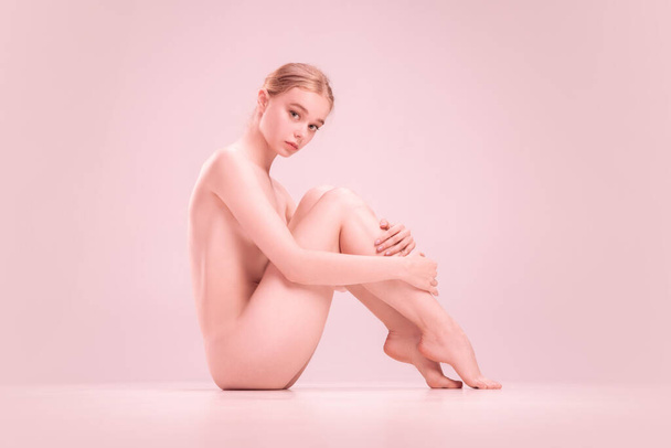 Slim young naked beautiful girl on pink background. Concept of beauty, purity, tenderness and grace. - Фото, зображення