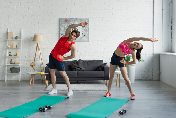 fit young couple in sportswear doing exercise near fitness mats before workout at home - Foto, imagen