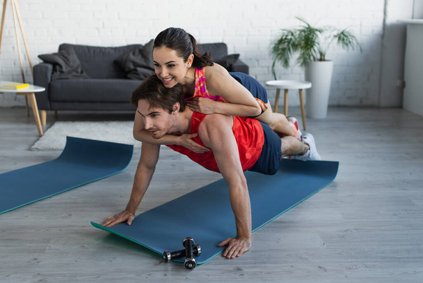 smiling fit young woman lying on back of man doing plank at home - Foto, imagen