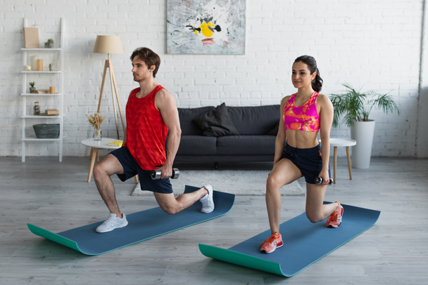 young couple in sportswear doing squats with dumbbells on fitness mats at home - Photo, Image