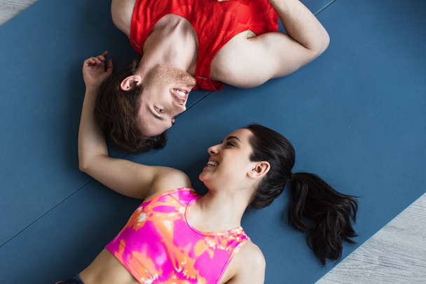 top view of young couple in sportswear lying on fitness mats and looking at each other at home - Foto, Imagem