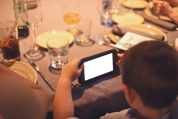 Child looking at cell phone screen at dinner time, educational concept - Foto, afbeelding