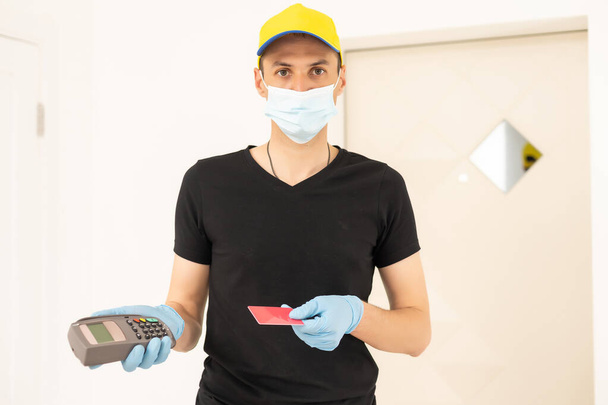 Delivery man holds bank payment terminal to process acquire credit card payments. Employee in cap t-shirt working courier. Service concept - Photo, Image
