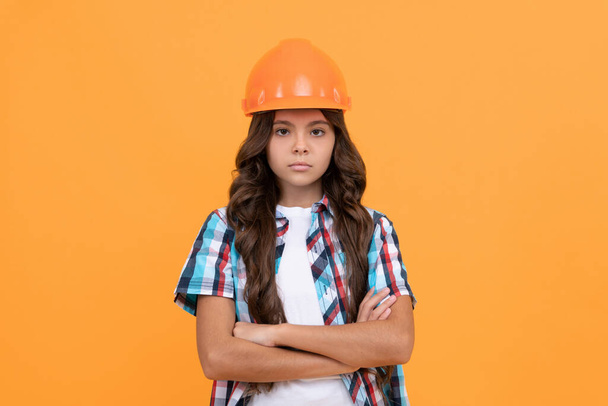 серьезный ребенок с вьющимися волосами в строительном шлеме, строитель - Фото, изображение