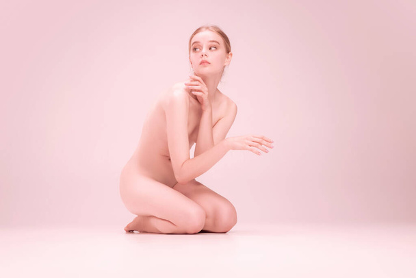 Young naked beautiful girl looking at camera isolated on pink studio background. Concept of beauty, purity, tenderness and grace. - Fotó, kép