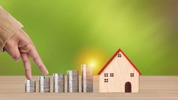 Концепція інвестицій у бізнес, чоловік рука ходить по монетах, зберігаючи зростання на дерев'яному столі з модельним будинком на зеленому фоні студії для фінансової реклами нерухомості
 - Фото, зображення