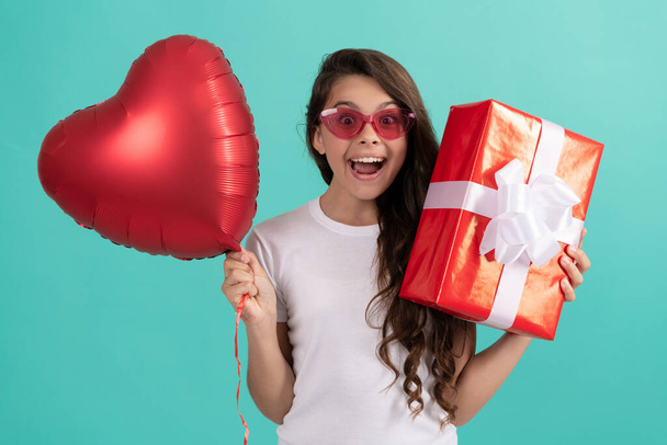 изумленный ребенок в очках держать подарочную коробку и валентинки день партии сердца воздушный шар, день любви - Фото, изображение