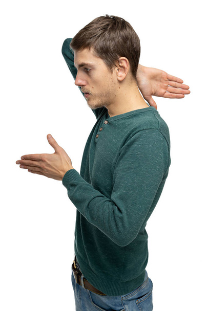 Young handsome tall slim white man with brown hair standing sideways in dark green sweater in blue jeans isolated on white background - Foto, afbeelding