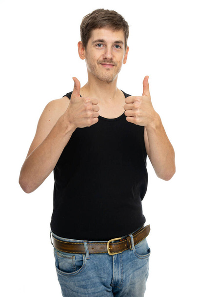Young handsome tall slim white man with brown hair thumbs up in black undershirt isolated on white background - Фото, изображение