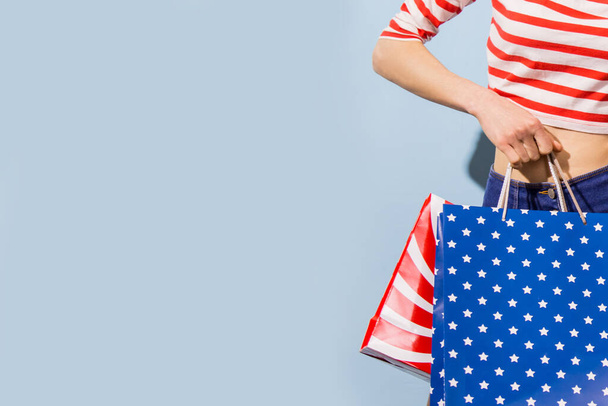 Happy shopping woman with shopping bags over blue background wearing striped clothing and shoping bags in patriotic colors - Photo, image