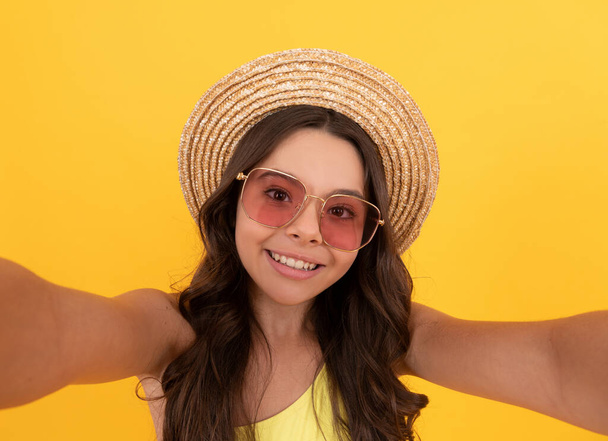 happy kid in summer straw hat and glasses making selfie on yellow background, summer selfie - Photo, Image