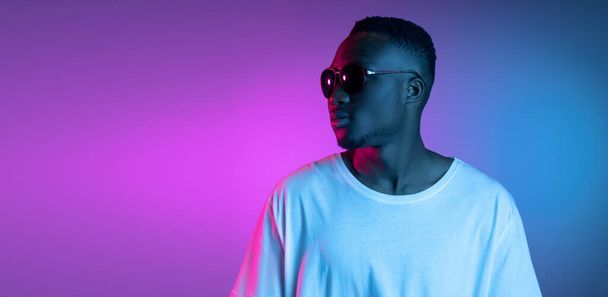 Young african man in sunglasses posing in neon light on gradient background. Concept of emotions, facial expression. - Фото, изображение