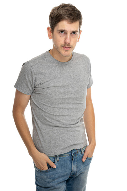 Young handsome tall slim white man with brown hair looking serious in gray shirt in blue jeans isolated on white background - Fotó, kép