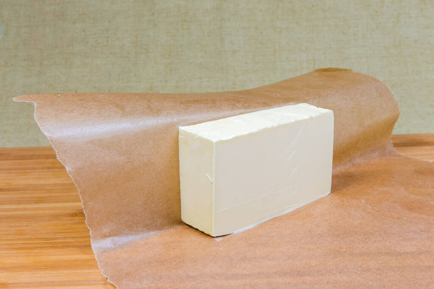 Pièce de beurre solide sur feuille de papier ciré sur une surface en bois - Photo, image