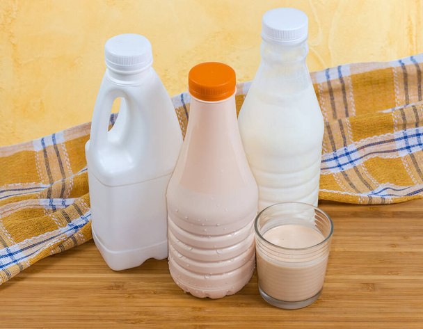 Fermented baked milk in glass against the plastic bottles of various dairy products on a wooden table with napkin  - Photo, Image