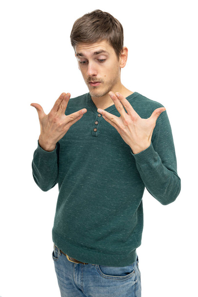 Young handsome tall slim white man with brown hair looking at his hands in dark green sweater in blue jeans isolated on white background - Fotó, kép