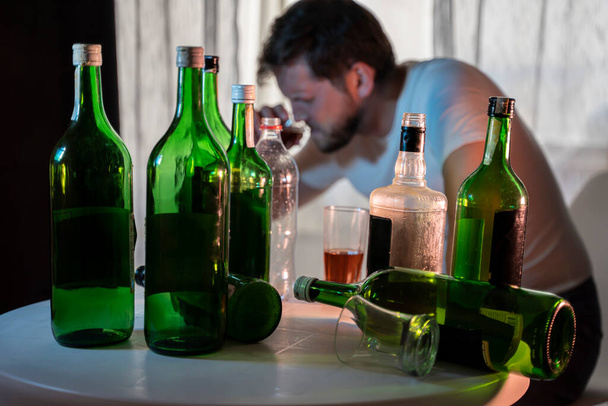 silhouette of an silhouette of an anonymous alcoholic drinking behind bottles of alcohol, alcoholism - Photo, Image