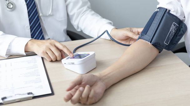 Male doctor uses a blood pressure monitor to check the body pressure and pulse of the patients who come to the hospital for check-ups, Medical treatment and health care concept. - Photo, Image