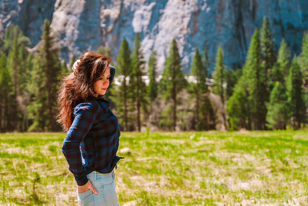 Uma jovem mulher bonita caminha por um vale verde no Parque Nacional de Yosemite com vista para as montanhas - Foto, Imagem